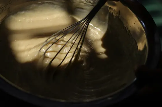 A balloon whisk drawing thick pale sauce up the side of a metal mixing bowl