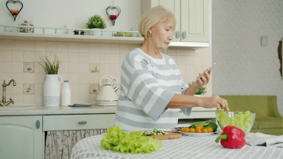 A person checking their phone while preparing salad in a bright kitchen