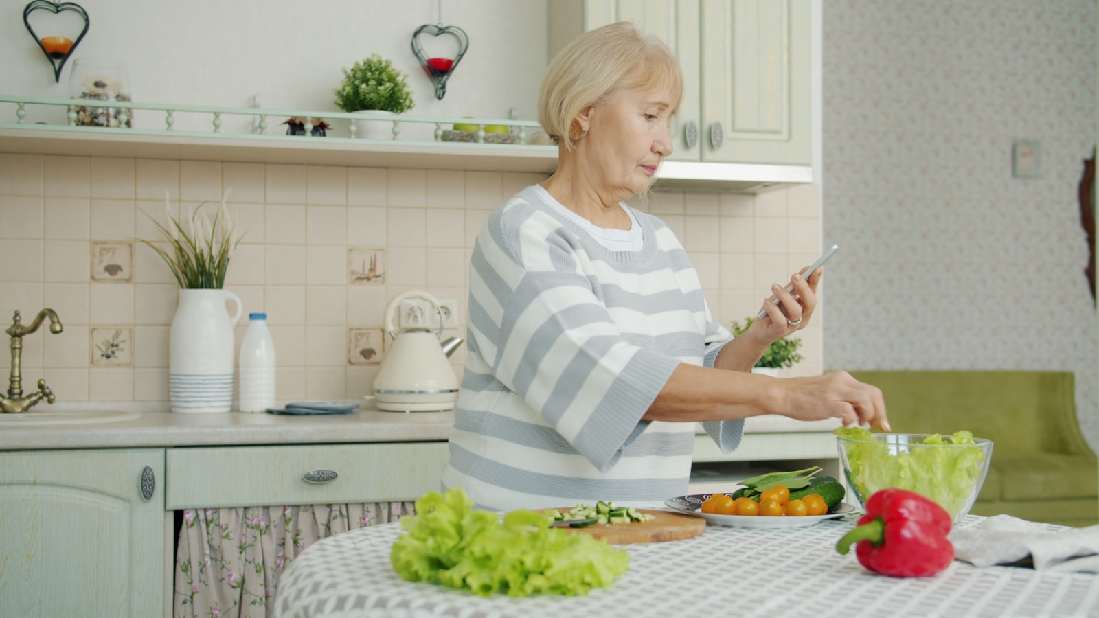 A person checking their phone while preparing salad in a bright kitchen