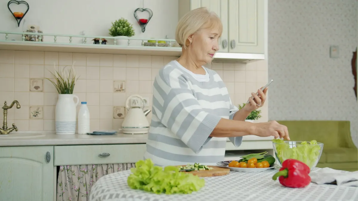 A person checking their phone while preparing salad in a bright kitchen