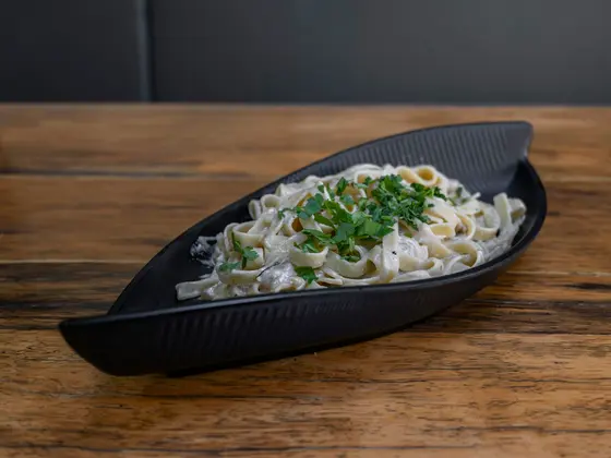 Fettuccine ribbons coated in a pale sauce and scattered with chopped parsley, served in a dark leaf-shaped dish on a wooden table