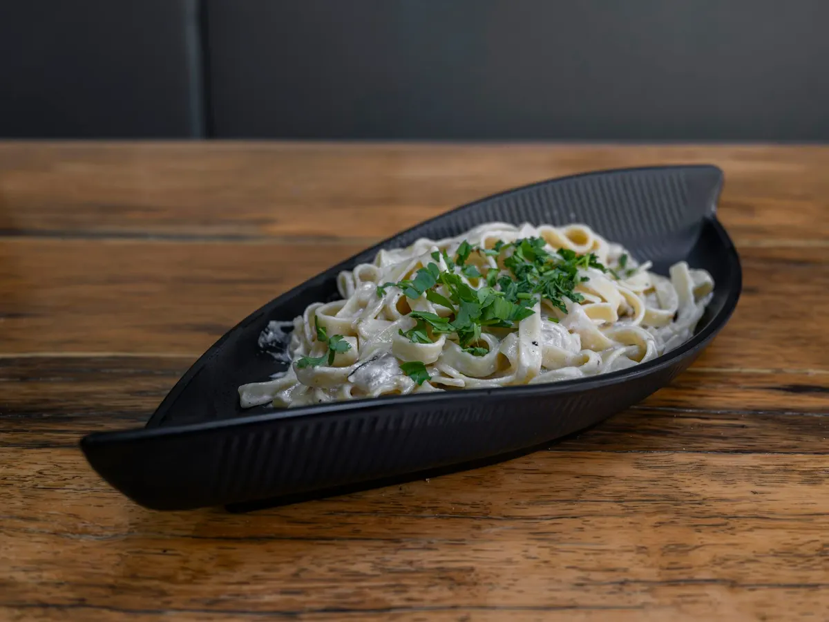 Fettuccine ribbons coated in a pale sauce and scattered with chopped parsley, served in a dark leaf-shaped dish on a wooden table