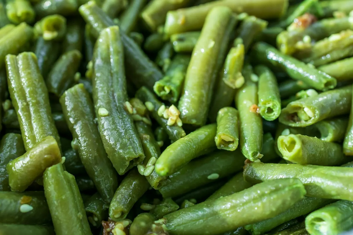 A close-up of cooked green beans, glossy from the pan and scattered with sesame seeds