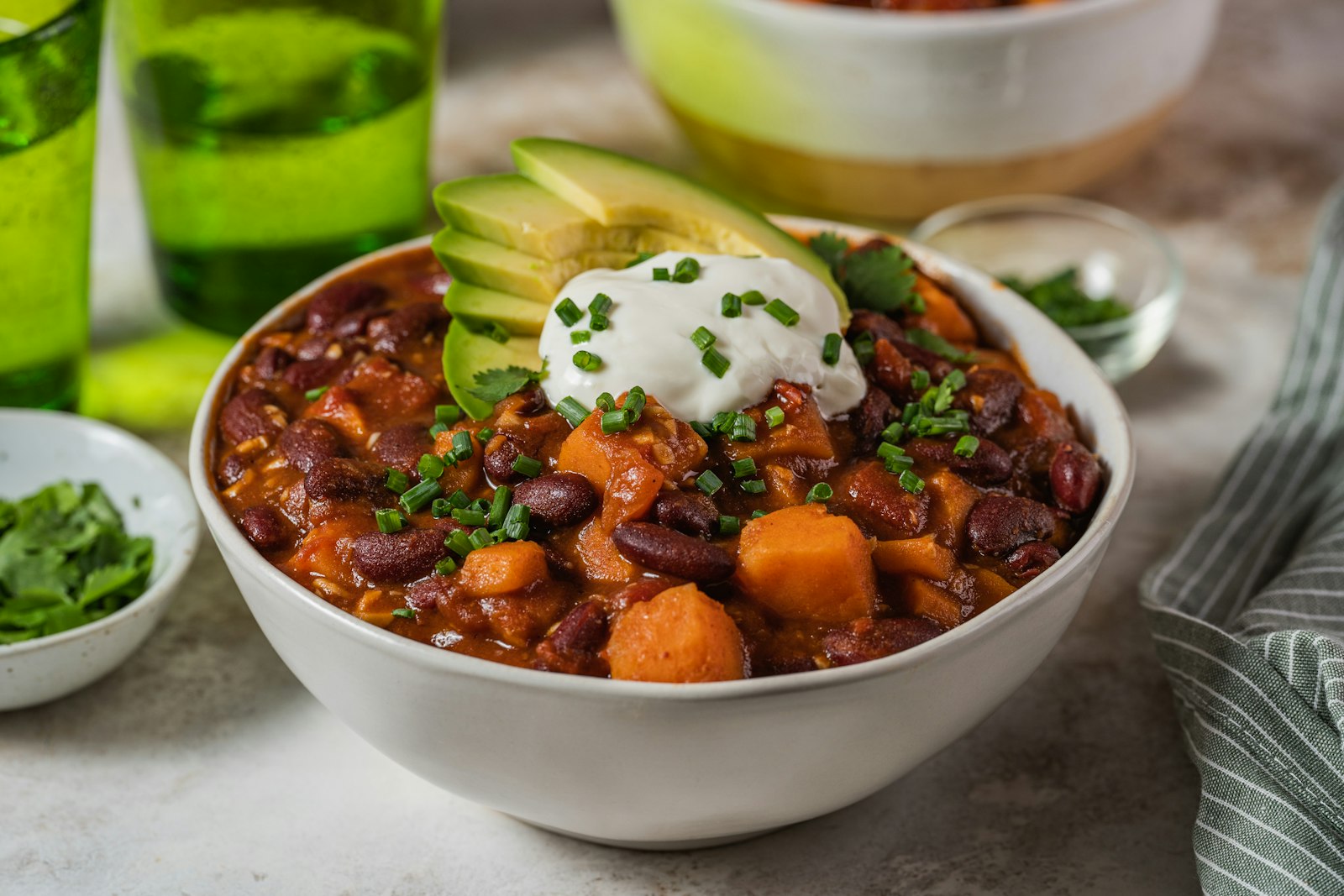A bowl of turkey chili with kidney beans and sweet potato, topped with sour cream, chives and sliced avocado