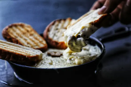 Toasted bread being dipped into a hot, bubbling cheese dip in a cast-iron pan