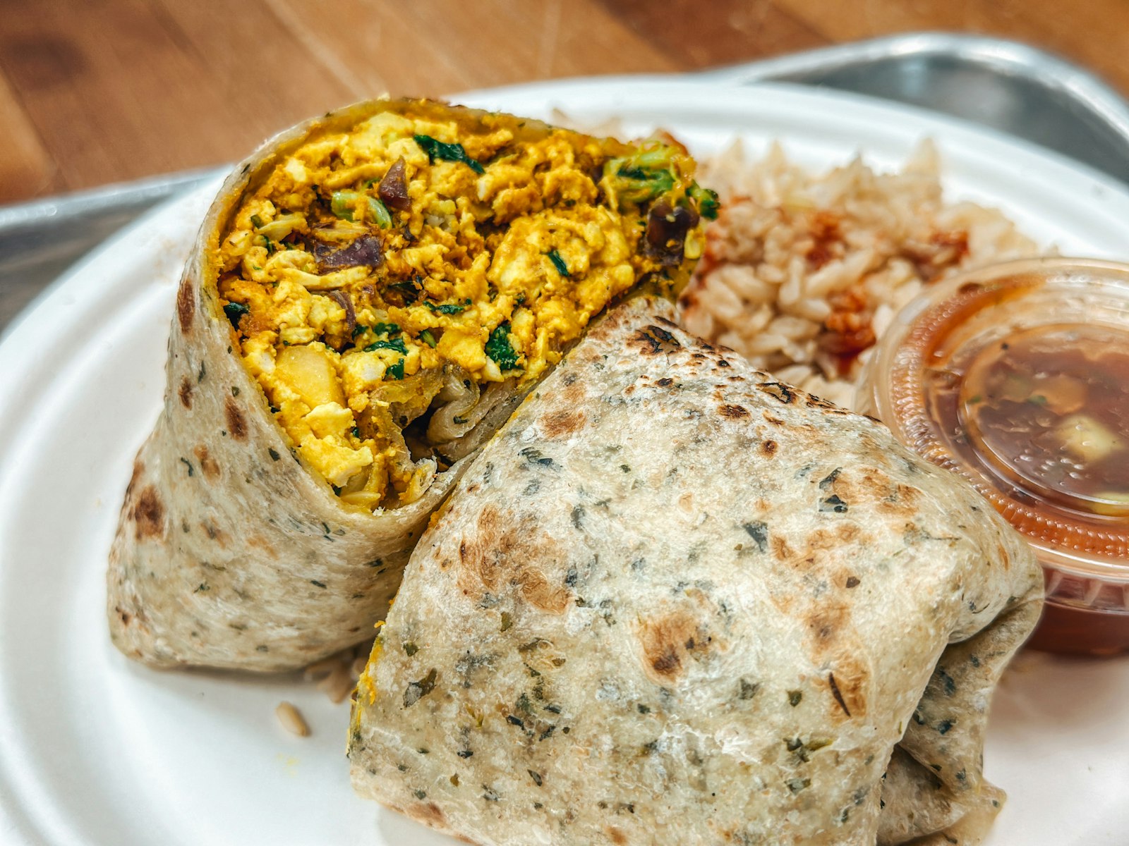 A breakfast burrito cut in half showing a scrambled egg and vegetable filling, served with rice and salsa