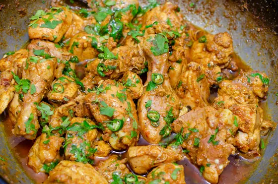Chunks of chicken in a shallow pan, coated in a thin spiced sauce with sliced green chillies and chopped coriander stirred through