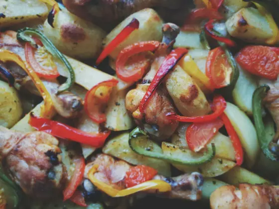 A tray packed with roasted chicken pieces, potato wedges and strips of red, green and yellow pepper with tomatoes