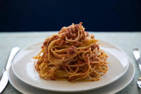 Spaghetti tossed with a minced meat sauce, piled on a white plate against a dark blue background