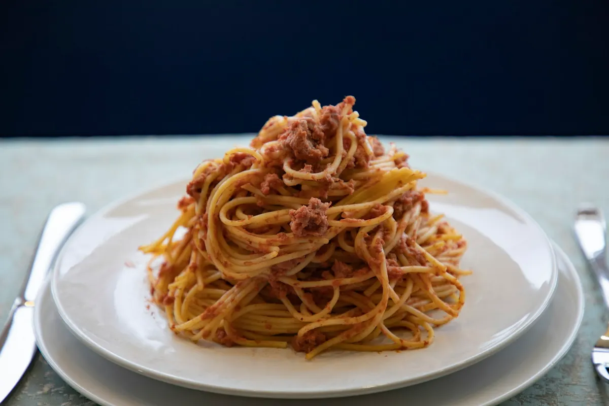 Spaghetti tossed with a minced meat sauce, piled on a white plate against a dark blue background