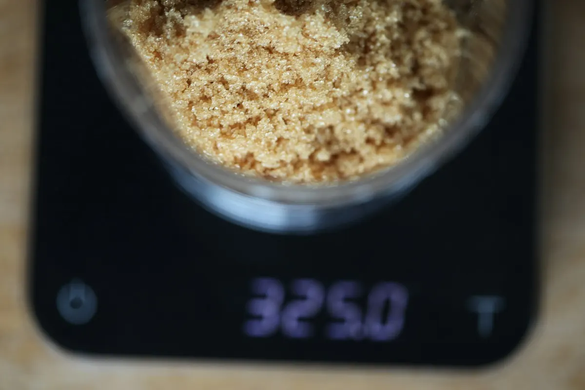 Light brown sugar in a glass bowl, being weighed on a black digital kitchen scale