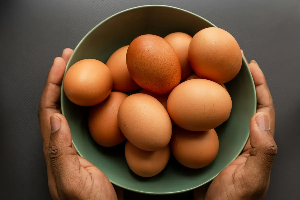 Two hands holding a green bowl filled with brown hen's eggs